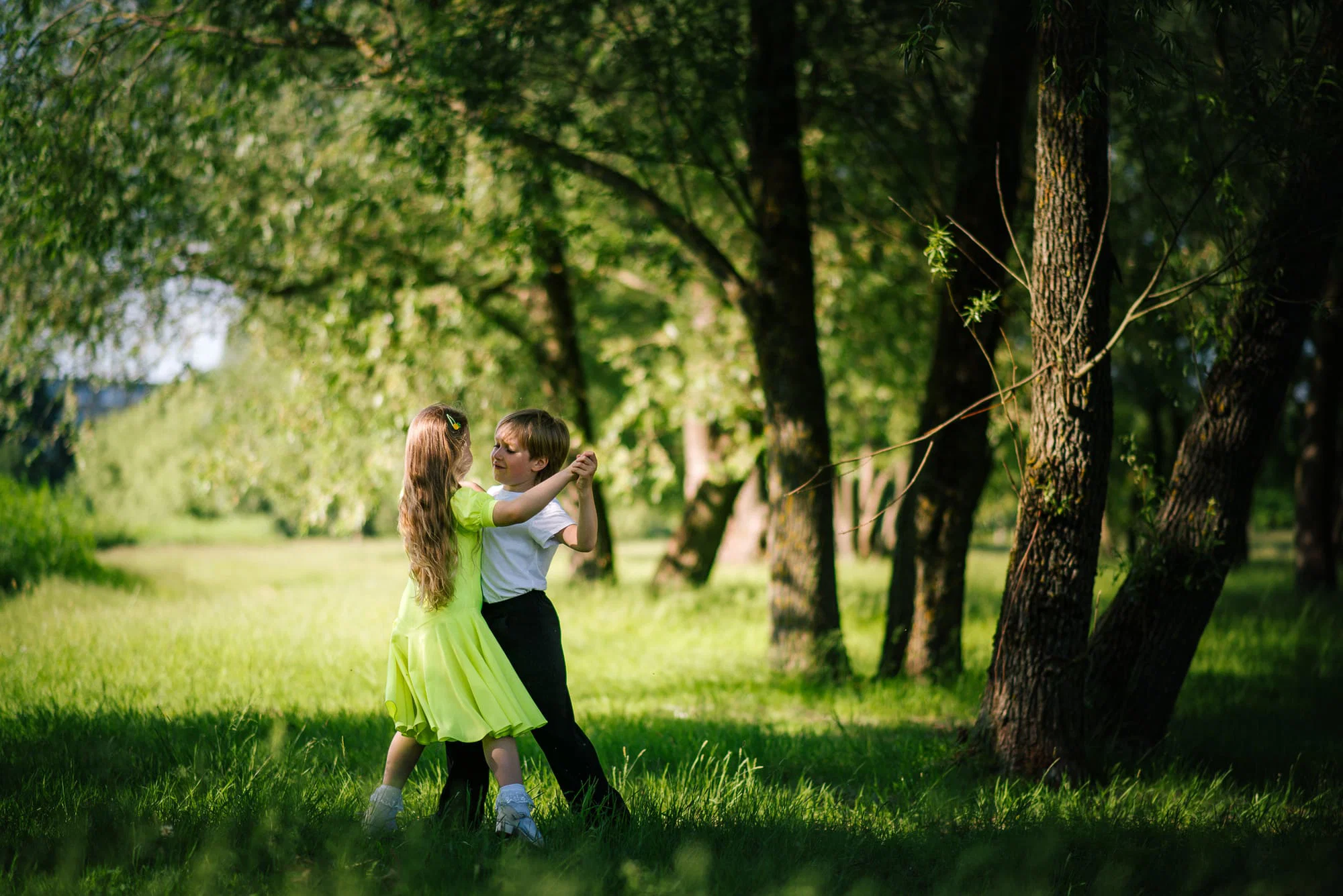 Mergaitė su berniuku šoka medžių pavėsyje, fotografė Kristina Boiko