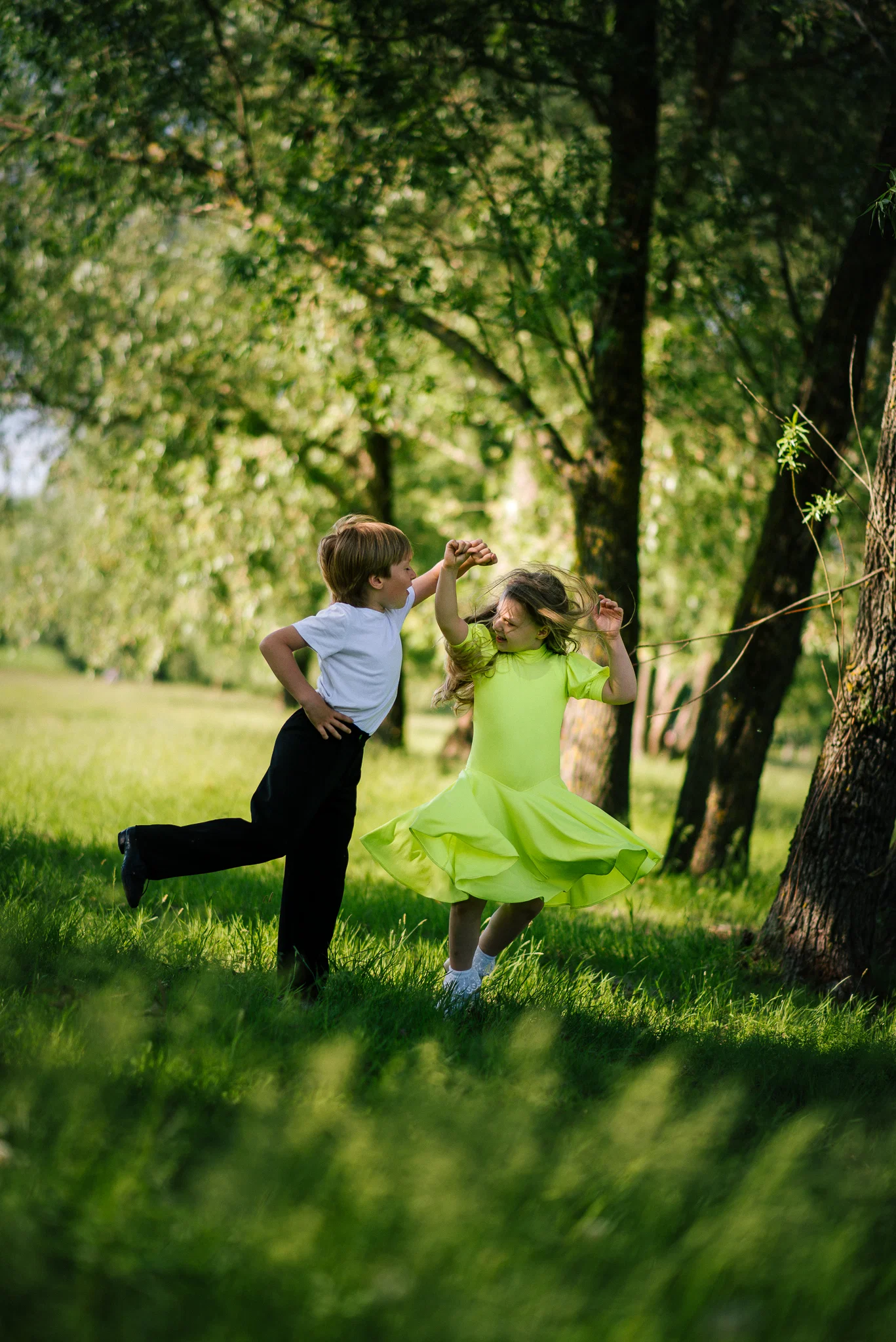 Mergaitė su berniuku šoka medžių pavėsyje, fotografė Kristina Boiko